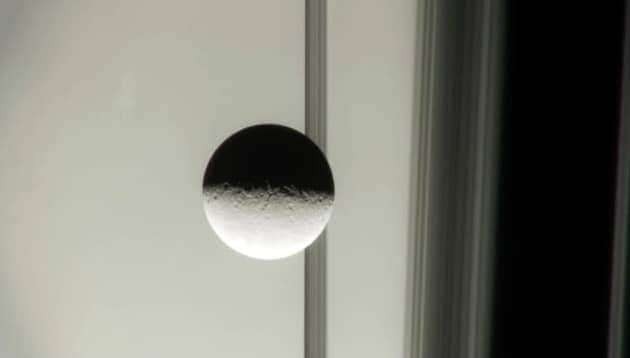 uma das luas de saturno contra os anéis do planeta