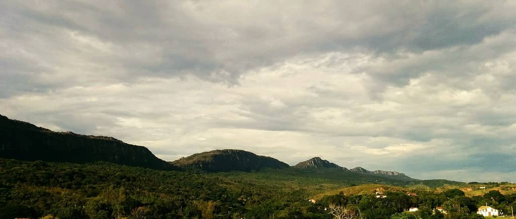 Conjunto de montanhase nuvens ao fundo, e cidade no primeiro plano