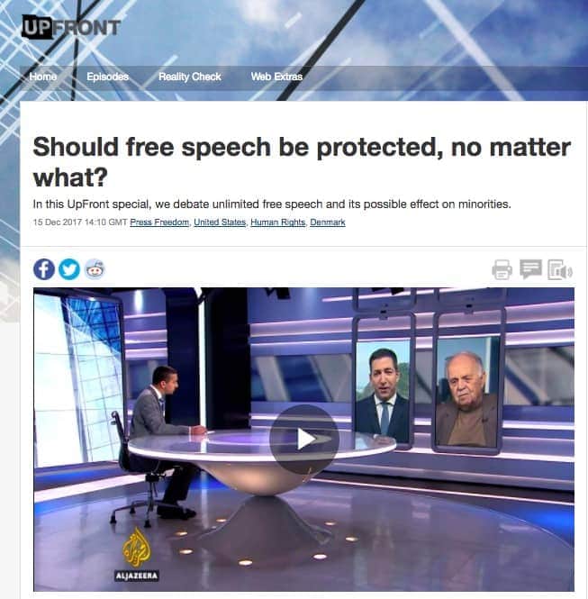 Jornalista em bancada conversando através de monitor com dois convidados