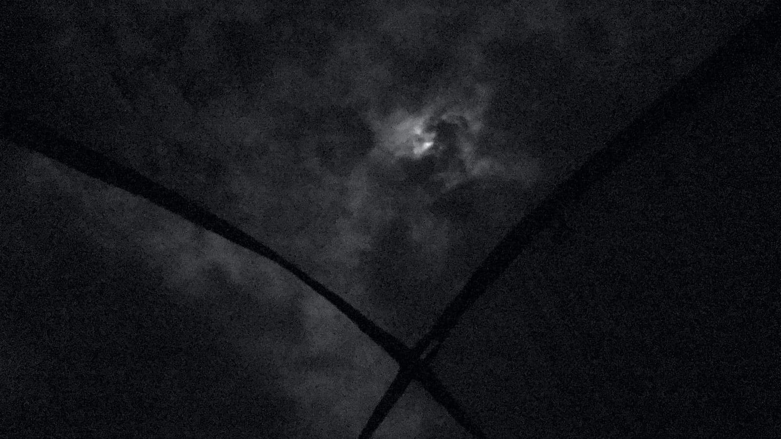 No centro, a lua no azimute entre nuvens em uma noite, vista através da tela no teto de uma barraca de camping, um pouco abaixo da lua, a estrutura da barra forma um X