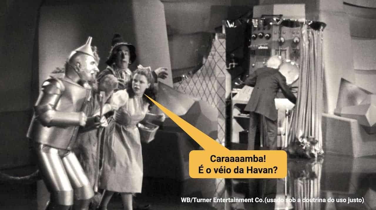 Texto sobre imagem. O texto, dentro de um "balão de díalogo", diz : Caraaaamba! É o véio da Havan? A imagem é uma cena, em preto e branco do filme O Mágico de Oz: Dorothy e seus companheiros, à esquerda, estão conversando, surpresos, e apontando para o homem por trás de uma cortina, movimentando uma máquina, sem se dar conta de que foi descoberto que é o manipulador do suposto Mágico de Oz.